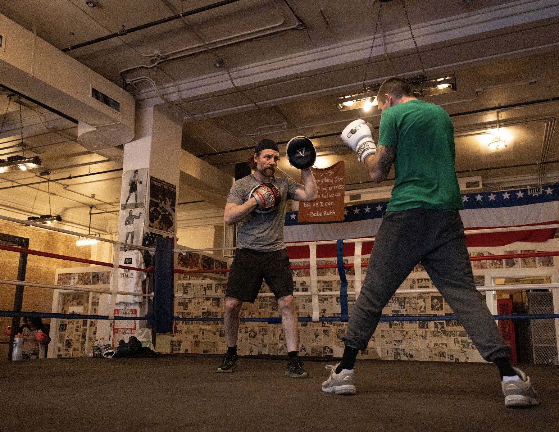 A Trinity boxing trainer holding focus pads for a member inside the ring